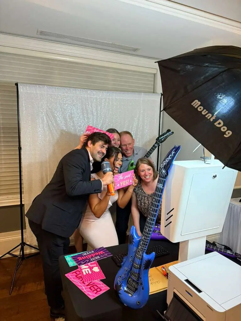 Wedding guests crowding into the photo booth with an inflatable guitar and signs